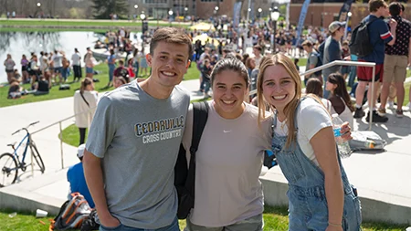 Three friends smiling together outside on campus.